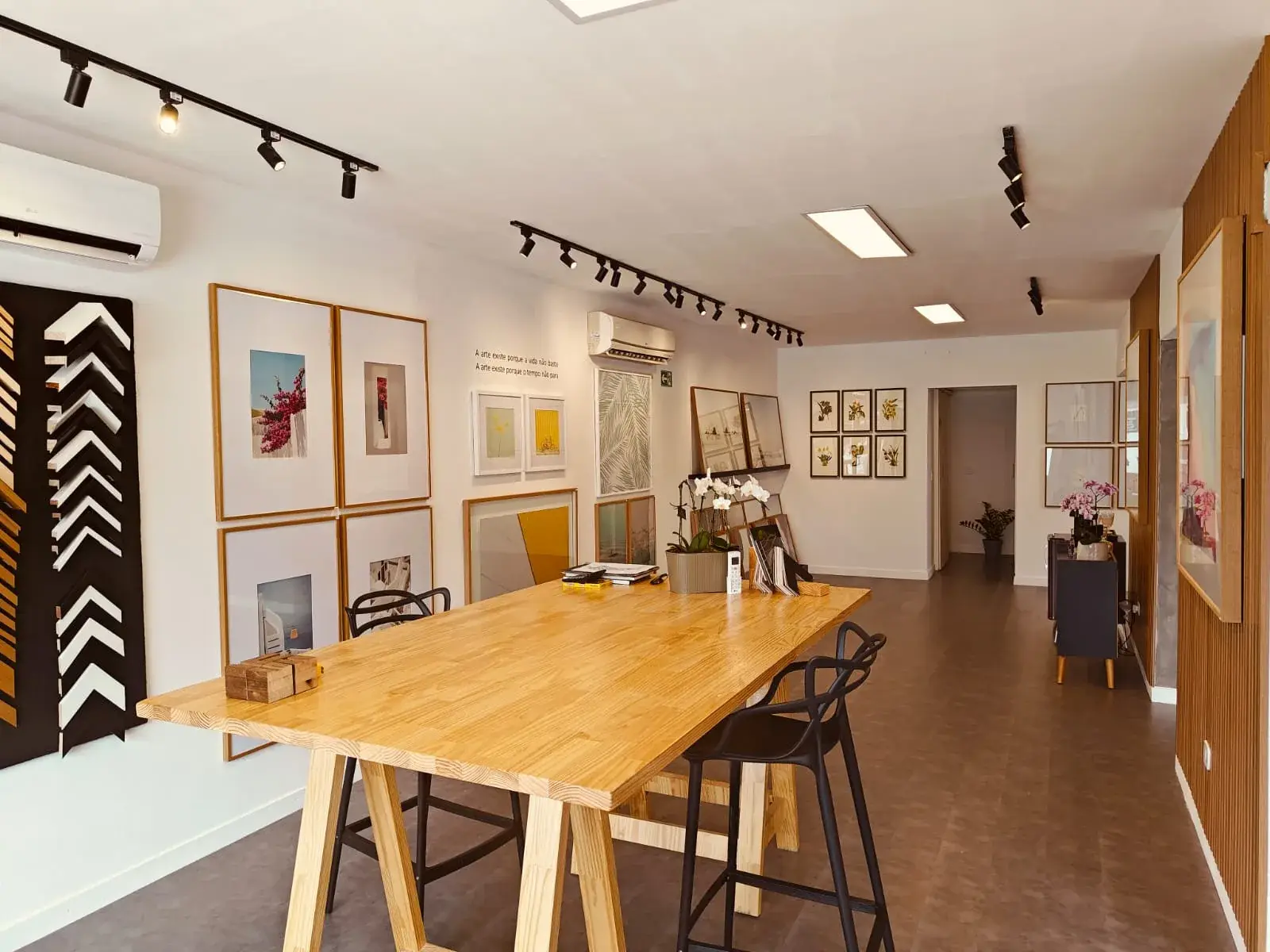 Interior da loja Moldura Minuto com parede-galeria de quadros e mesa de consultoria