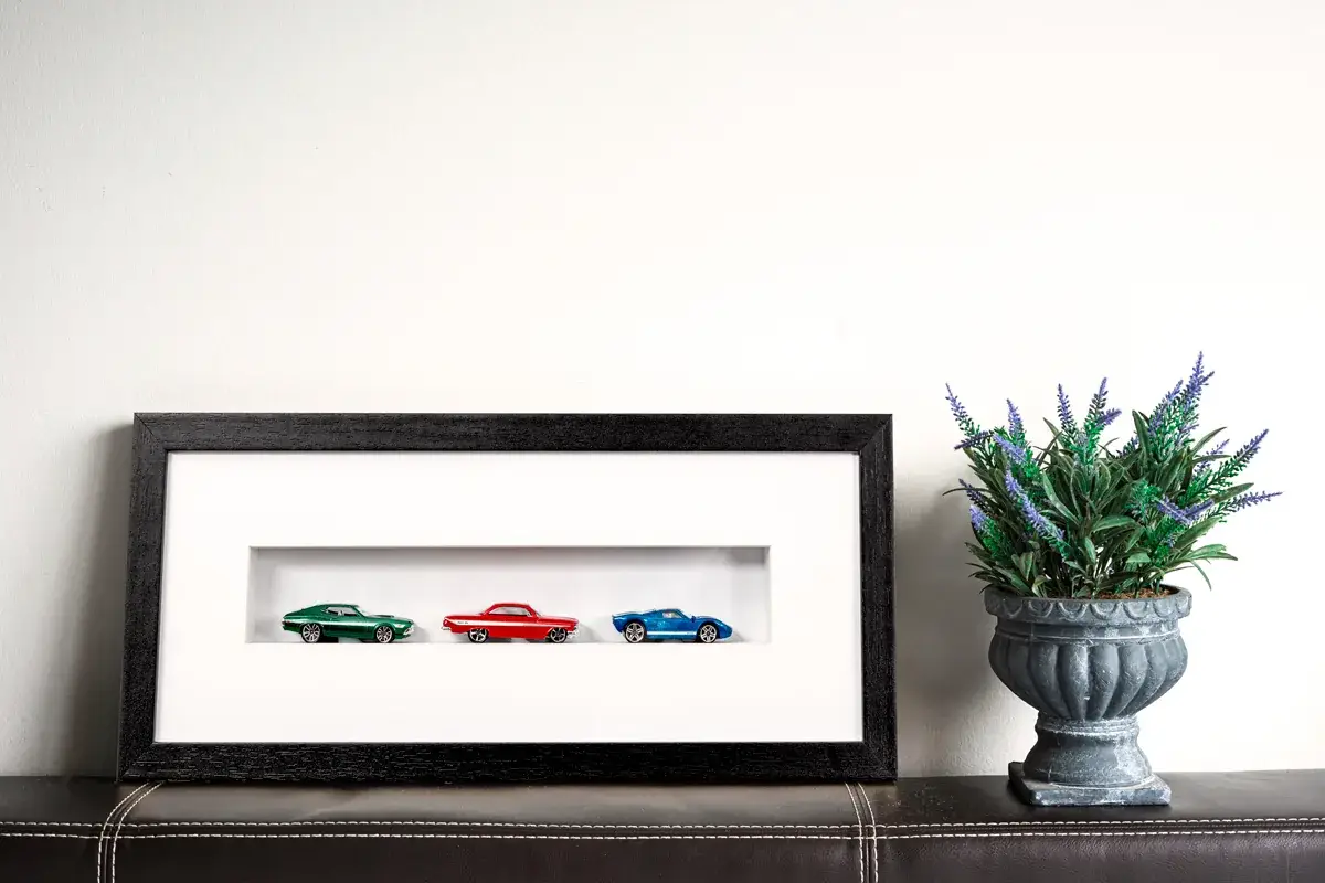 Três miniaturas de carros emolduradas em caixa preta